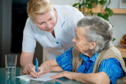 The caregiver is helping the old woman to write down notes