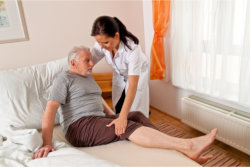 The caregiver helps the old man to lay down properly